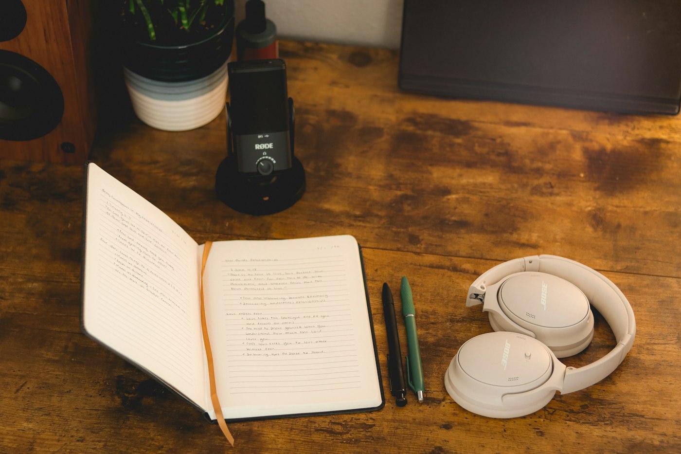 Open notebook, pens and headphones on a rustic wooden desk for guided audio meditations